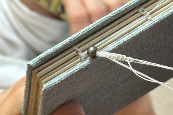 Na zdjęciu widać odkryty fragment grzbietu ręcznie szytego notesu, wykonanego ręcznie w jasnoniebieskiej okładce.