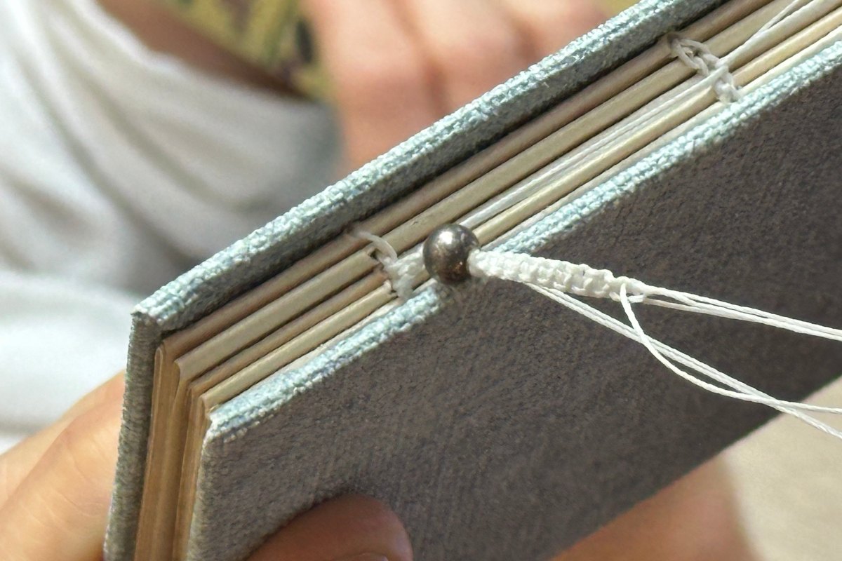 Na zdjęciu widać odkryty fragment grzbietu ręcznie szytego notesu, wykonanego ręcznie w jasnoniebieskiej okładce.